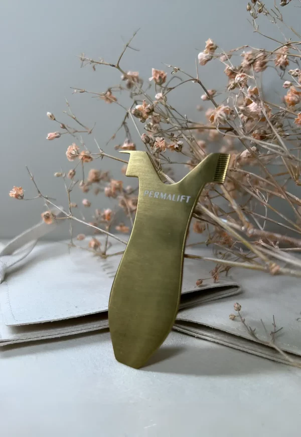 Permalift 3-in-1 Y-comb standing among dried flowers, highlighting its gold finish and precision design for lash lift treatments