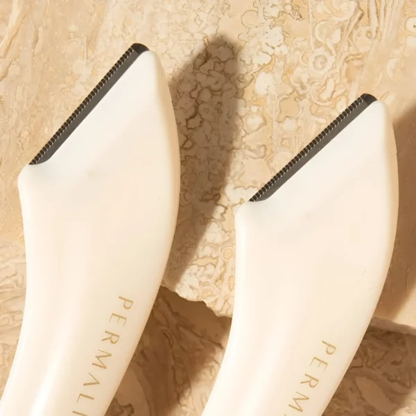 Close-up of two Permalift Brow Razors, showcasing their ergonomic design and high-quality blades on a textured beige background for precise brow shaping