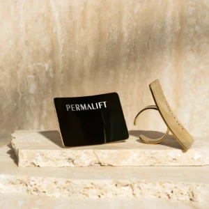 Two permalift gold colored mixing rings with branding displayed on a stone surface, with soft, natural lighting highlighting the products.